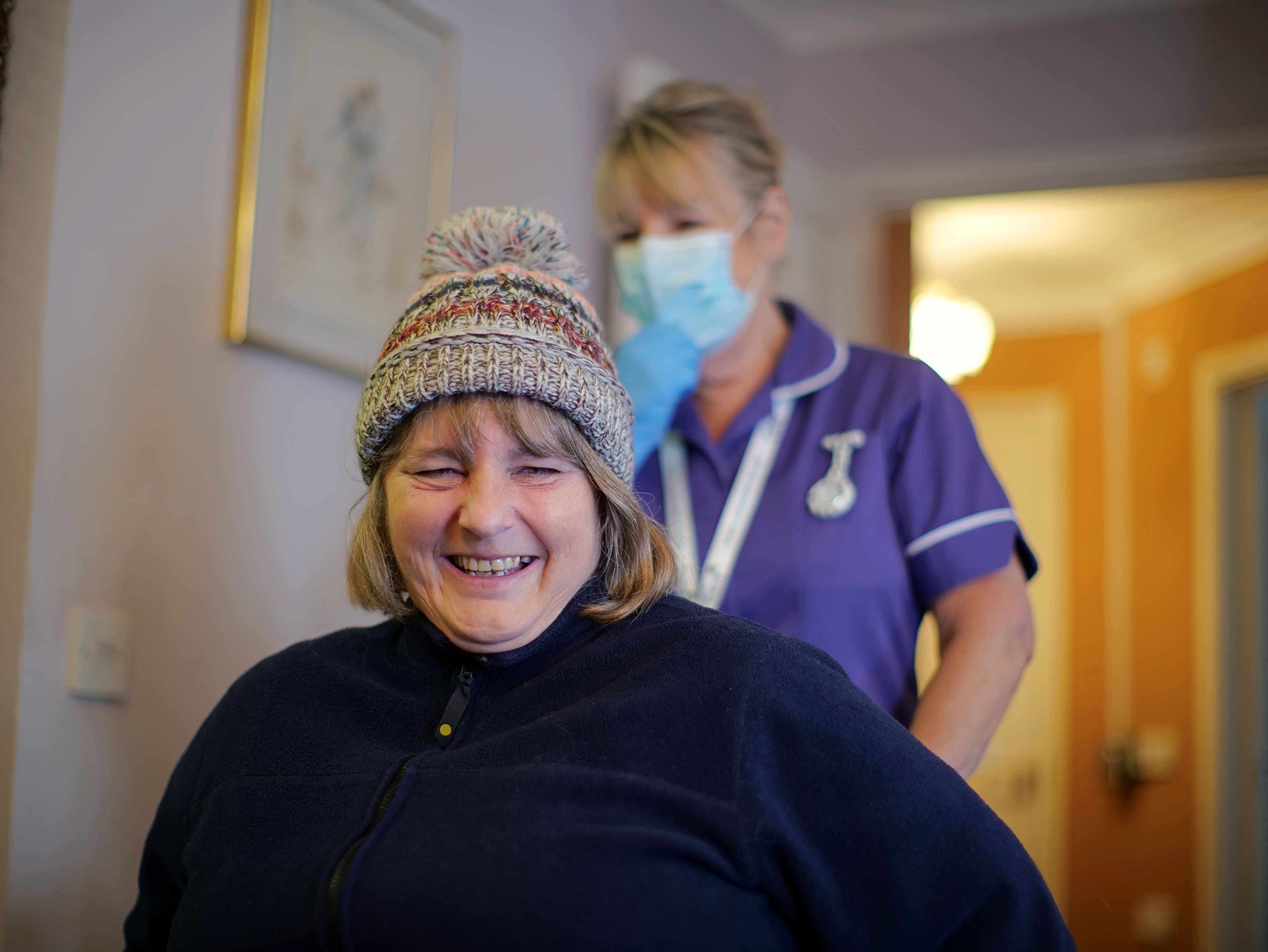 Winter service user in winter hat smiling and carer behind